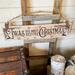 A handmade Christmas sign. Old time writing has been wood-burned onto a piece of reclaimed wood. Reindeer and holly are on either side. 